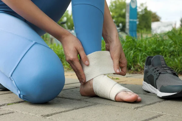 Woman wrapping foot in medical bandage outdoors, closeup