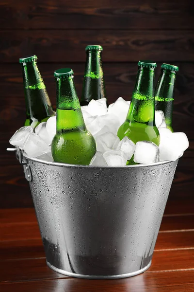 Metal bucket with bottles of beer and ice cubes on wooden table