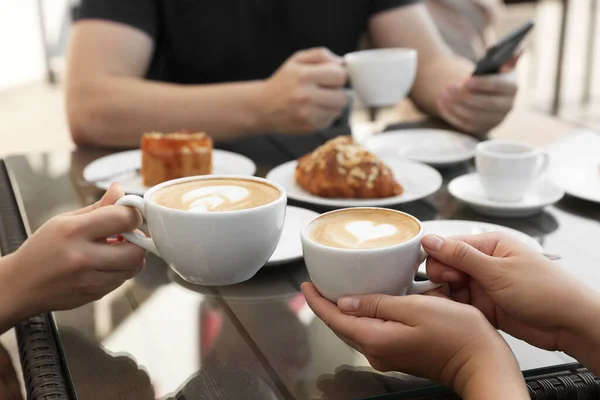 Friends drinking coffee at wooden table in outdoor cafe, closeup