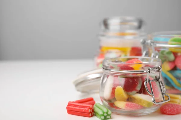 Tasty jelly candies in jars on white table, space for text