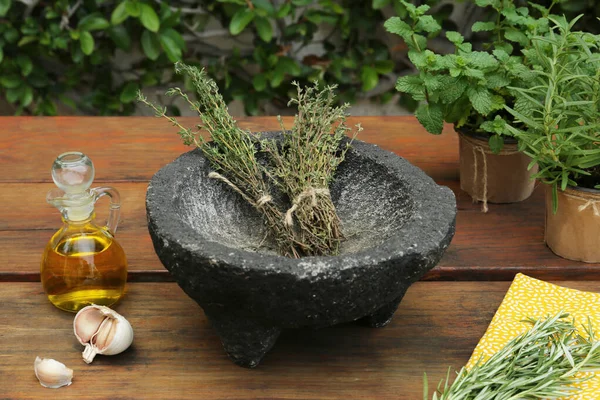 Mortar, different herbs, garlic and oil on wooden table