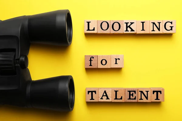 Staff recruitment concept. Phrase Looking For Talent made of wooden cubes and binoculars on yellow background, flat lay