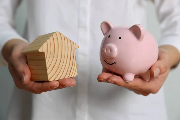 Woman holding piggy bank and house model on white background, closeup