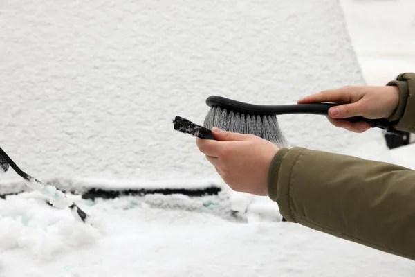 Woman cleaning car wiper blade from snow with brush, closeup