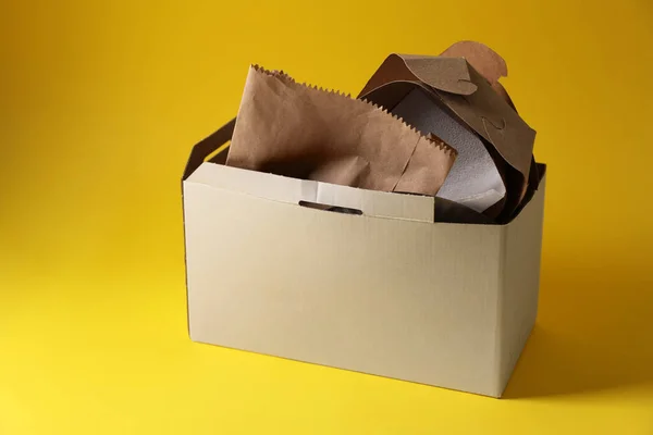 Box with waste paper on yellow background