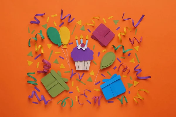 Birthday party. Paper cupcake, air balloons and gifts on orange background, flat lay