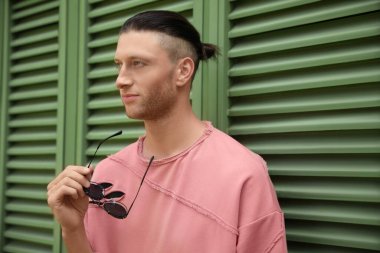 Panjurların yanında şık güneş gözlüklü yakışıklı bir genç.