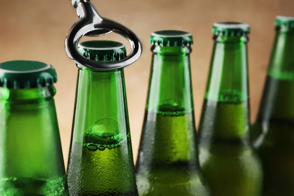 Opening bottle of beer on light brown background, closeup. Space for text