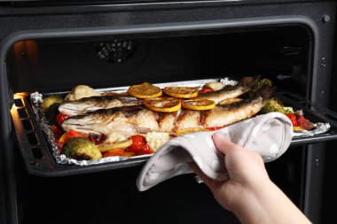 Fırından deniz levreği ve sebzelerle fırın tepsisi alan kadın, yakın plan.