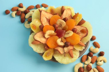 Açık mavi arka planda karışık kurutulmuş meyve ve fındık, yakın plan.