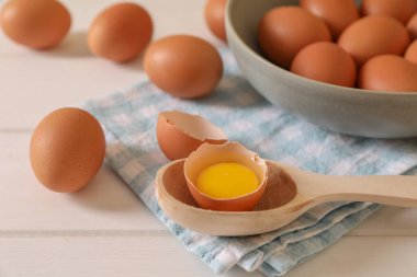 Taze çiğ tavuk yumurtası, kase, kaşık ve peçete beyaz ahşap masa, yakın plan.