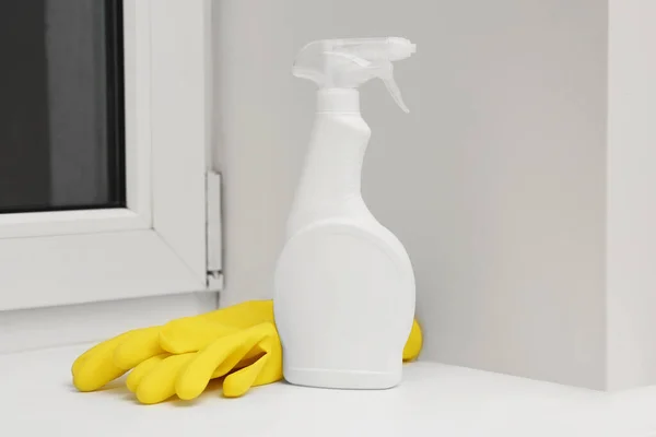 Spray bottle of cleaning product and rubber gloves on window sill indoors