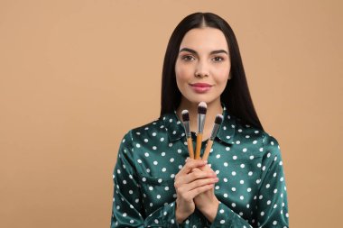 Açık kahverengi arka planda farklı makyaj fırçaları olan güzel bir kadın. Metin için boşluk