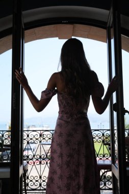 Genç bir kadın balkonda dikiliyor.