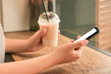 Kafede pencerenin yanında akıllı telefon kullanan kadın, yakın plan.