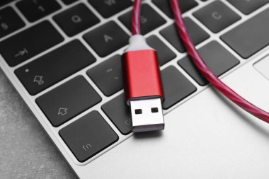 Gri masada kırmızı USB kablo ve laptop, yakın plan.