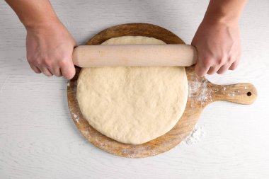 Beyaz masadaki ahşap broşlu hamuru yuvarlayan adam.