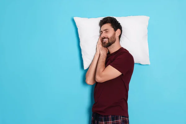 Sleepy handsome man with pillow on light blue background, space for text