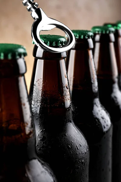 Opening bottle of beer on light brown background, closeup