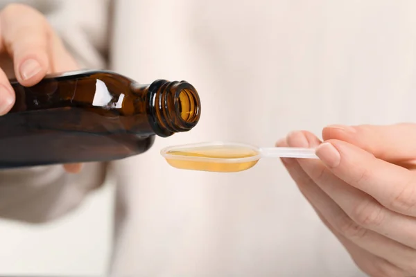 Woman pouring syrup from bottle into dosing spoon, closeup. Cold medicine