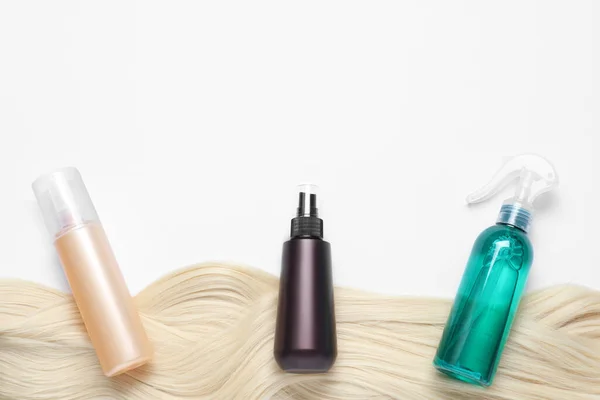 Spray bottles with thermal protection and lock of blonde hair on white background, flat lay. Space for text