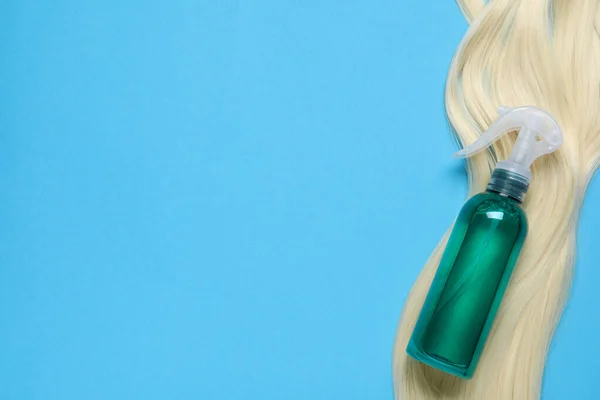 Spray bottle with thermal protection and lock of blonde hair on light blue background, flat lay. Space for text