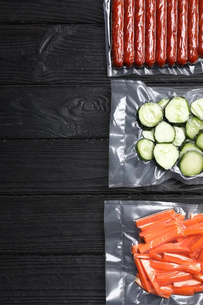 Tasty food in vacuum packings on black wooden table, flat lay. Space for text