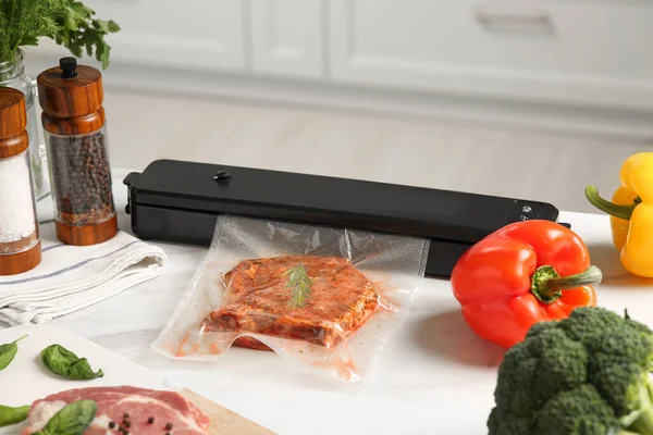 Sealer for vacuum packing with meat in plastic bag on white kitchen table