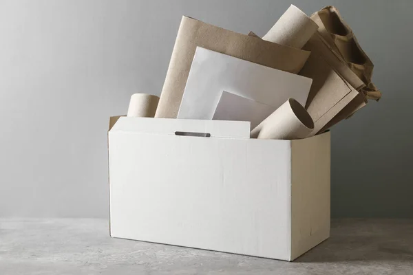 Box with different waste paper on grey table