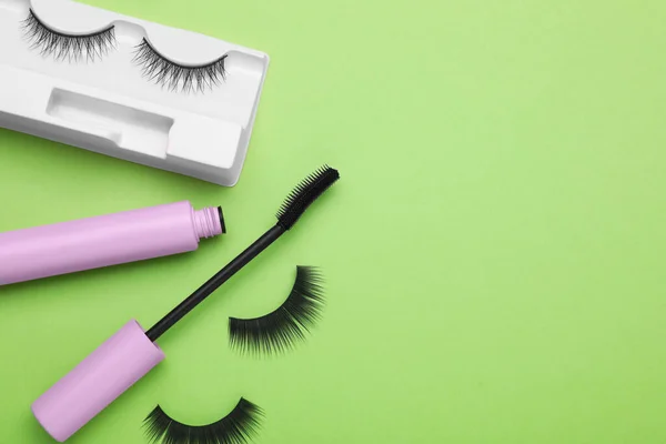 Flat lay composition with fake eyelashes and mascara brush on green background. Space for text