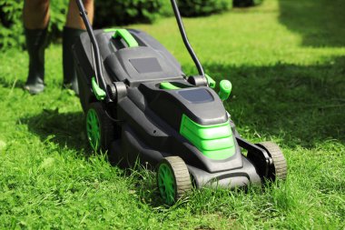 Güneşli bir günde bahçede çim biçme makinesiyle çim biçen adam, yakın plan.