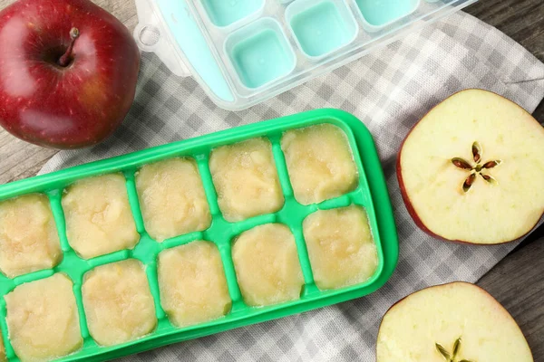 Apple puree in ice cube tray with ingredients on table, flat lay
