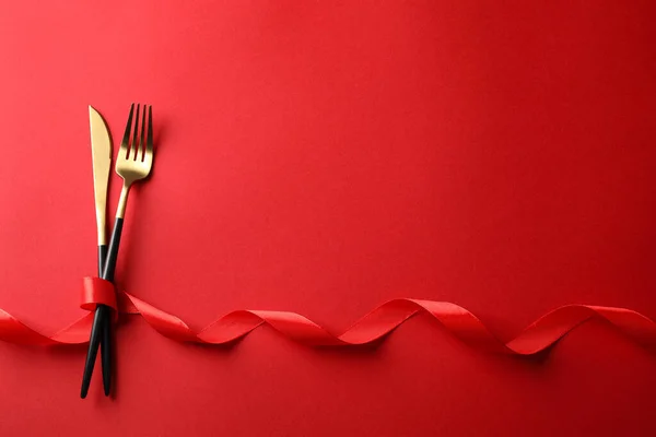Cutlery set and ribbon on red background, flat lay with space for text. Romantic table setting