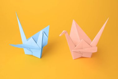 Origami sanatı. Turuncu arka planda güzel açık mavi ve soluk pembe kağıt turnalar.