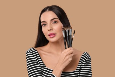 Açık kahverengi arka planda farklı makyaj fırçaları olan güzel bir kadın.