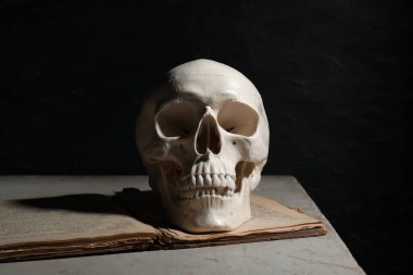İnsan kafatası ve eski kitap siyah arka plana karşı masada