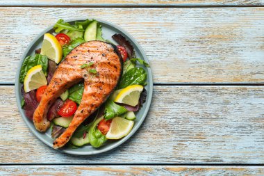 Beyaz ahşap masada limonlu ve sebzeli somon bifteği, üst manzara. Metin için boşluk