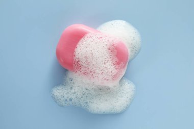 Açık mavi arka planda yumuşak köpüklü sabun çubuğu, üst görünüm