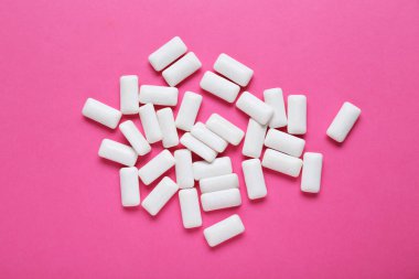 Pembe arka planda dişetleri çiğneyen lezzetli beyaz sakızlar.