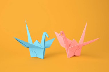 Origami sanatı. Turuncu arka planda güzel açık mavi ve soluk pembe kağıt turnalar.
