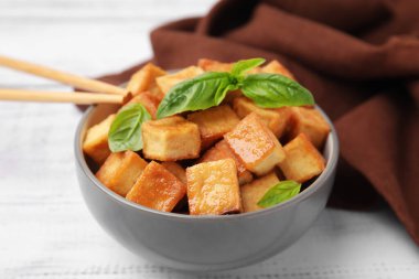 Lezzetli kızarmış tofu ve fesleğenli kase beyaz masada, yakın plan.