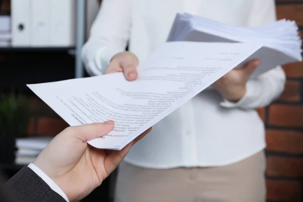 Woman giving many documents to man in office, closeup