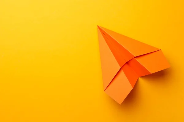 Handmade orange paper plane on yellow background, top view. Space for text
