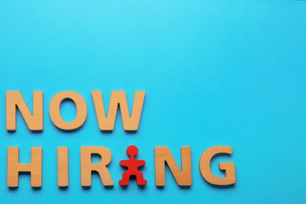Recruitment process. Phrase Now Hiring made of wooden letters and red human figure on light blue background, flat lay