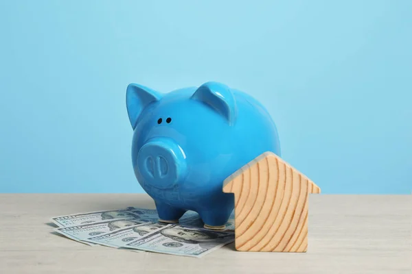 Piggy bank, house model and banknotes on white wooden table