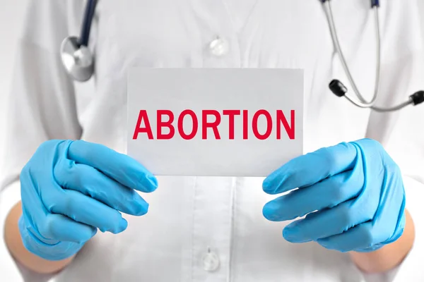 Doctor holding paper card with word Abortion, closeup