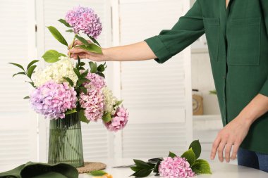 İçerideki masada ortanca çiçekleriyle buket yapan bir kadın, yakın plan. İç tasarım ögesi