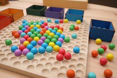 Wooden sorting board and boxes with colorful balls on table, closeup. Montessori toy