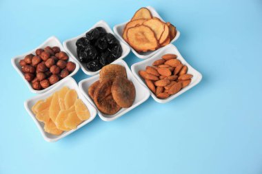 Açık mavi arka planda kurutulmuş meyve ve fındıklı kaseler, metin için boşluk