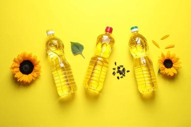 Sarı arka planda yemek yağı, ayçiçeği ve tohum şişeleri düzdü.